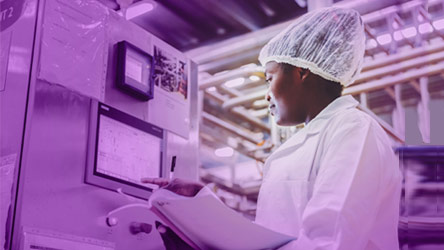 Техник в лабораторна престилка работи с контролен панел в производствена среда, фокусирайки се върху качествен контрол.