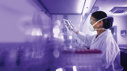 Лаборантка с маска и престилка работи с пипета в лаборатория, демонстрирайки прецизност и безопасност.