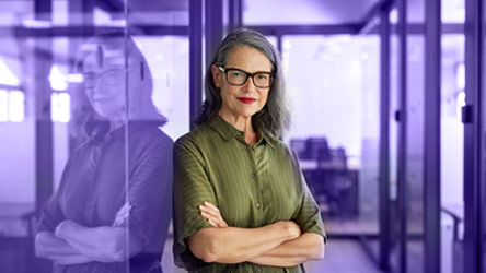 Уверена бизнес дама с кръстосани ръце, стои пред офис със стъклени стени, излъчвайки професионализъм и опит.