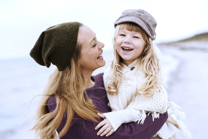 Усмихната майка прегръща дъщеря си на открито, символ на радост и семейна връзка.