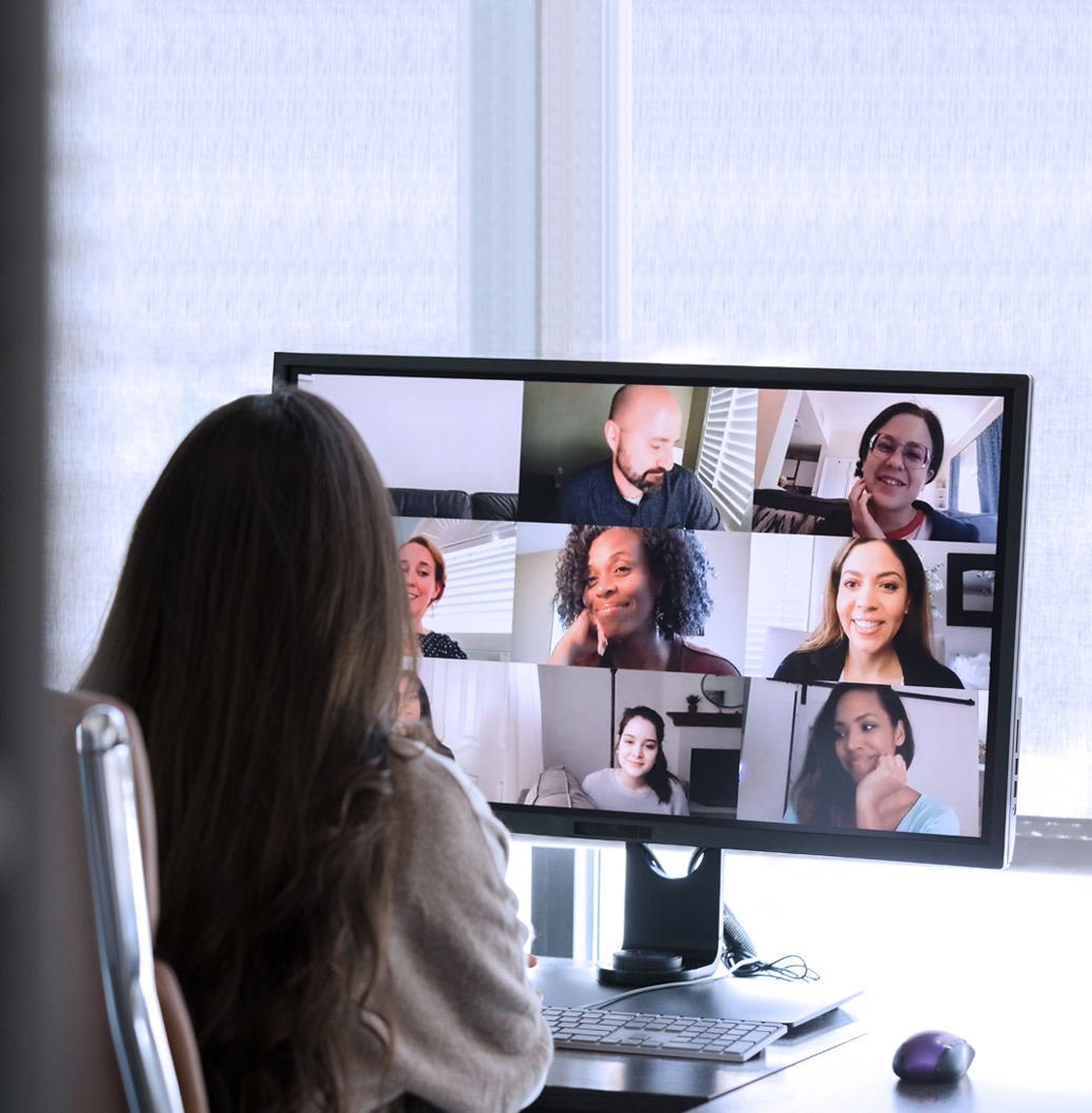 Жена участва във видеоконференция с колеги, показани на екрана в мрежа от девет лица.