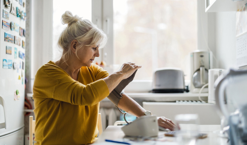 Възрастна жена измерва кръвното си налягане у дома, показвайки грижа за здравето си в спокойна домашна обстановка.